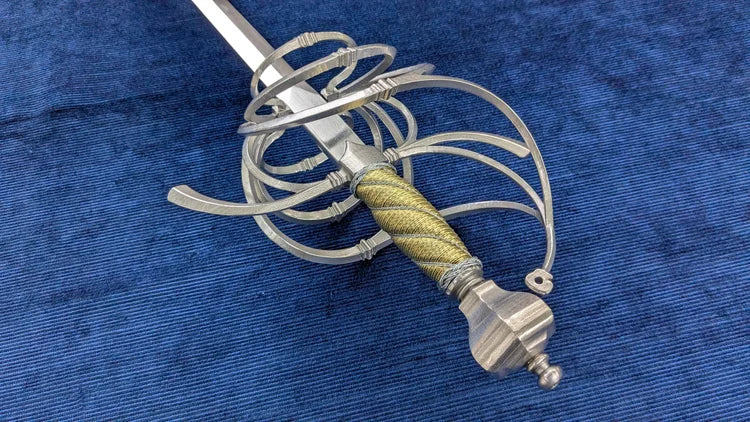 A medieval-style sword with a silver-colored metal guard, a textured gold and silver wrapped hilt, and a silver pommel, displayed diagonally on a blue textured fabric background.