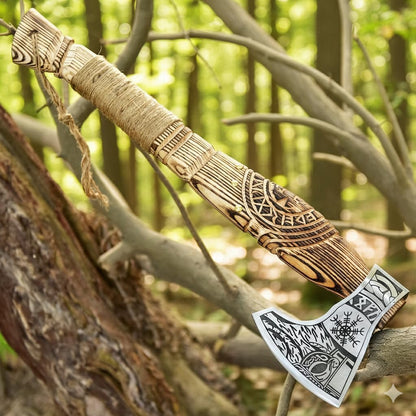 Decorative axe with intricate designs hanging on a tree branch in a forest setting