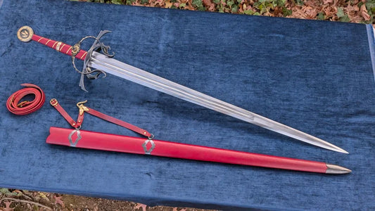 A medieval-style sword with a red wrapped hilt and silver blade, displayed diagonally on a blue textured cloth alongside a matching red scabbard and red leather strap.
