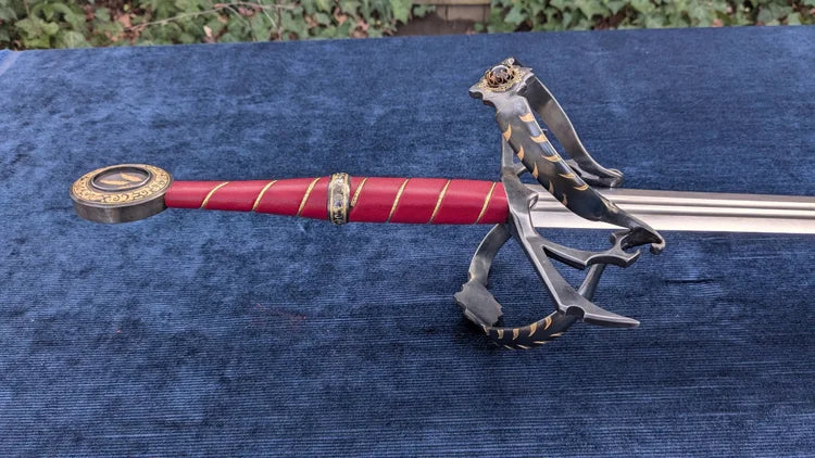 A decorative sword with a red wrapped handle, gold accents, and a silver blade, displayed on a blue textured surface with a dragon figurine holding the hilt.