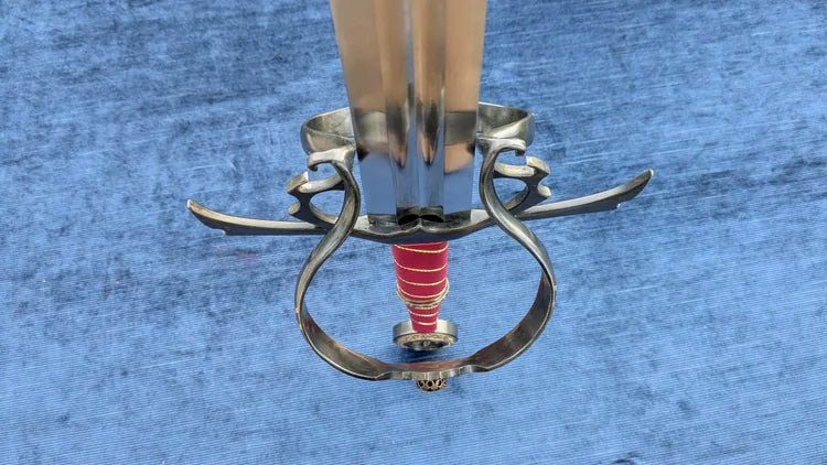 A close-up of a decorative sword hilt with a polished silver guard and pommel, a red wrapped grip, and a light-colored blade, set against a textured blue background.