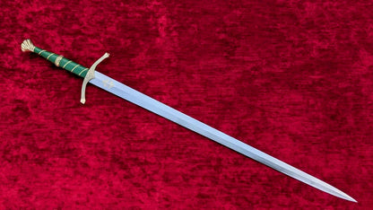 A medieval-style sword with a silver blade, gold guard and pommel, and a green wrapped handle, displayed diagonally on a textured red velvet background.