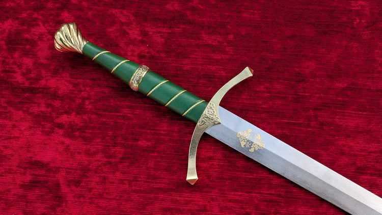A decorative sword with a green wrapped handle, gold accents, and a silver blade, displayed diagonally on a textured red velvet background.
