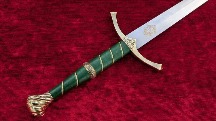 A decorative sword with a green wrapped handle and ornate gold-colored guard and pommel, displayed diagonally on a textured red velvet background.