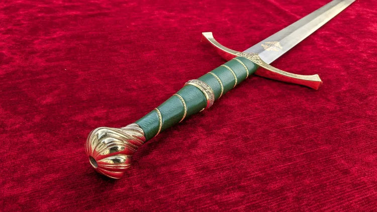 A medieval-style sword with a green leather-wrapped handle and gold-colored metal fittings, resting diagonally on a textured red velvet background.