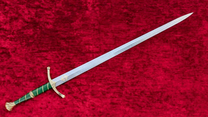 A medieval-style sword with a silver blade, green wrapped hilt, and gold guard and pommel, displayed diagonally on a textured red velvet background.