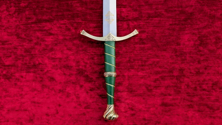 A decorative sword with a silver blade, gold guard and pommel, and a green wrapped hilt, displayed vertically on a textured red velvet background.