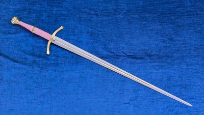 A medieval-style sword with a pink grip and gold guard, displayed diagonally on a textured blue fabric background.