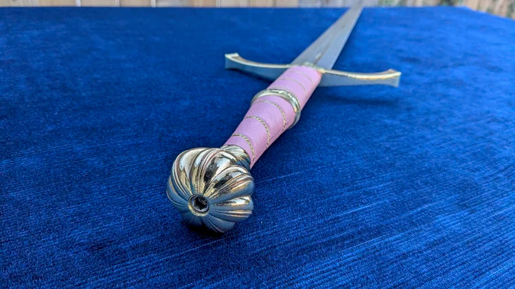 A decorative sword with a pink wrapped handle and silver-colored metal guard and pommel, resting on a textured blue fabric surface.