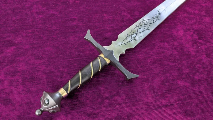 A fantasy-style sword with a silver engraved blade, a dark wrapped hilt, and gold accents, displayed diagonally on a textured purple velvet background.
