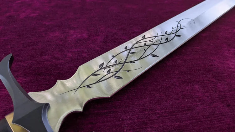 A close-up of a fantasy-style sword with a silver blade featuring black engraved vine and leaf patterns, resting on a textured deep purple velvet background.