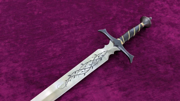 A fantasy-style sword with a silver blade featuring black engraved leaf patterns, a black crossguard, and a black wrapped hilt with gold accents, displayed diagonally on a textured magenta velvet background.