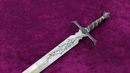 A fantasy-style sword with a silver blade featuring black engraved leaf patterns, a black crossguard, and a black wrapped hilt with gold accents, displayed diagonally on a textured magenta velvet background.