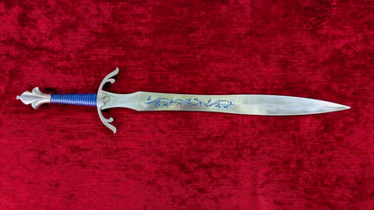 A medieval-style short sword with a silver-colored blade featuring blue floral engravings, a blue wrapped grip, and a silver guard, displayed horizontally on a textured red velvet background.