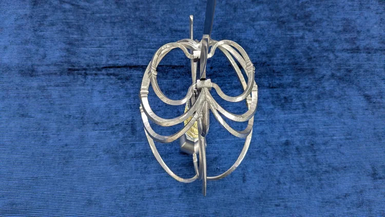 A silver metal cage-style guard, likely for fencing or equestrian use, displayed against a textured blue background.