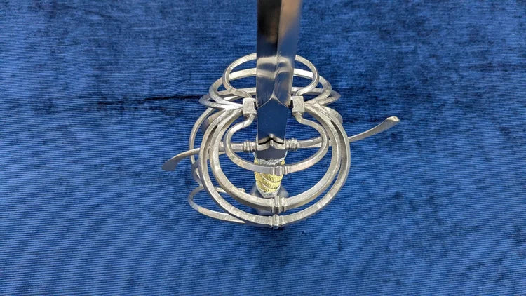 A silver metal spiral cage or basket-like tool with a vertical handle, photographed on a textured blue fabric background.