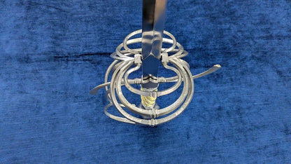 A silver metal spiral cage or basket-like tool with a vertical handle, photographed on a textured blue fabric background.