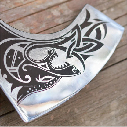Decorative metal axe head with intricate black patterns on a wooden surface