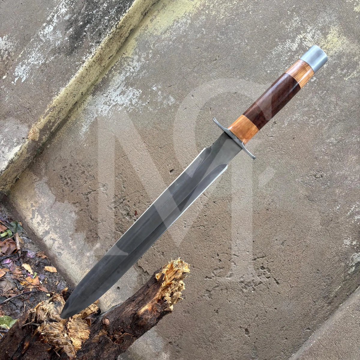 A fixed-blade knife with a dark gray steel blade, a brown and orange wood-grain handle, and a silver pommel, shown resting on a concrete surface.