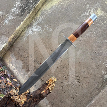 A fixed-blade knife with a dark gray steel blade, a brown and orange wood-grain handle, and a silver pommel, shown resting on a concrete surface.