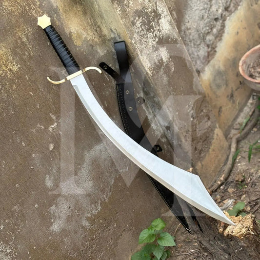 A curved sword with a silver blade, black wrapped handle, and gold guard, shown with a black sheath on a weathered stone surface outdoors.