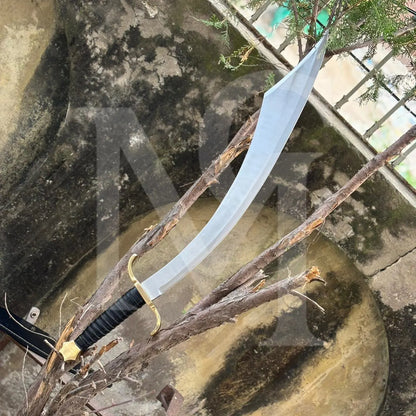 A curved sword with a silver blade, black wrapped handle, and gold guard is displayed resting on tree branches outdoors.