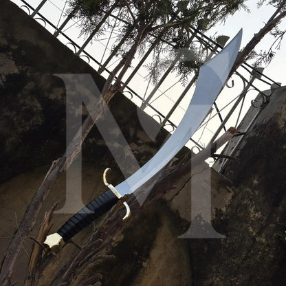 A curved sword with a silver blade, black wrapped handle, and gold guard, displayed outdoors against a rustic stone wall and metal fence.
