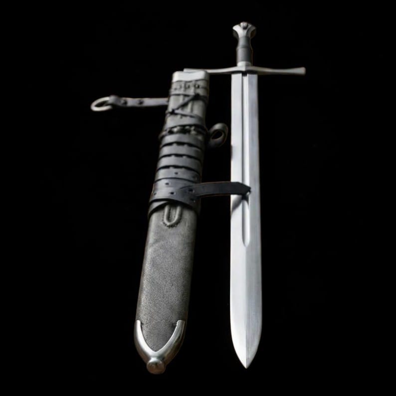 Medieval longsword displayed beside its leather scabbard showing the blade, crossguard, and handle
